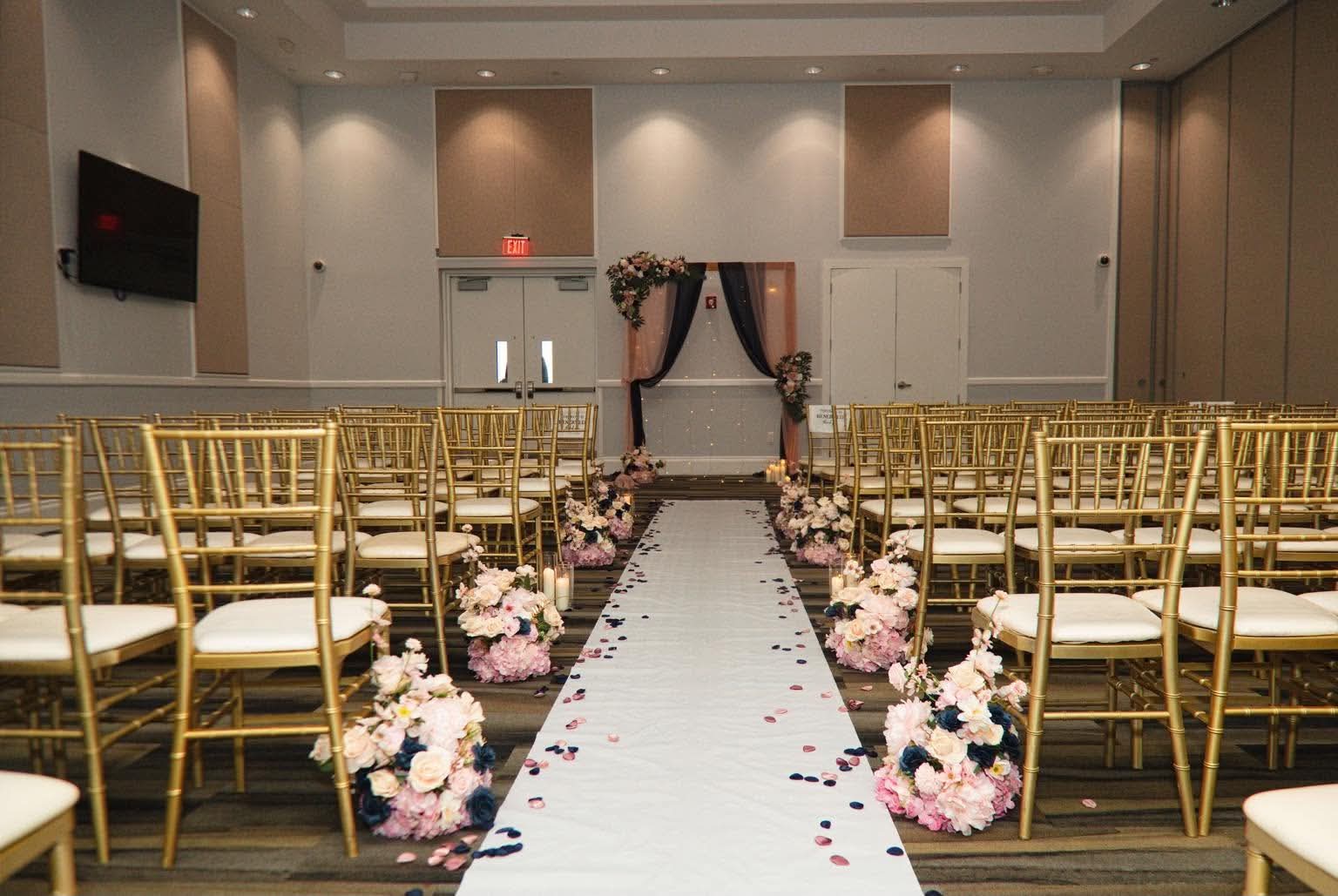 Wedding ceremony aisle lined with blush flowers, candles, and gold chairs