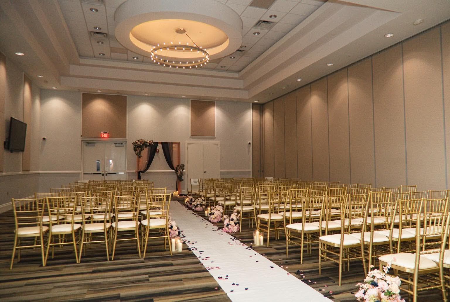 Wedding ceremony ballroom with gold chairs and a floral aisle